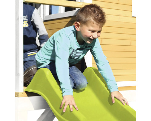 Junge rutscht auf einer grünen Rutsche an einem Spielhaus