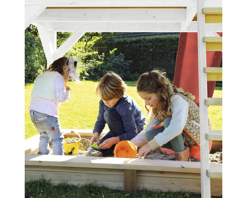 Drei Kinder spielen im Sandkasten unter einem Spielturm im Garten.
