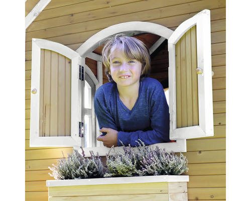 Junge schaut aus dem Fenster eines Holzspielhauses mit Fensterkasten und Bepflanzung