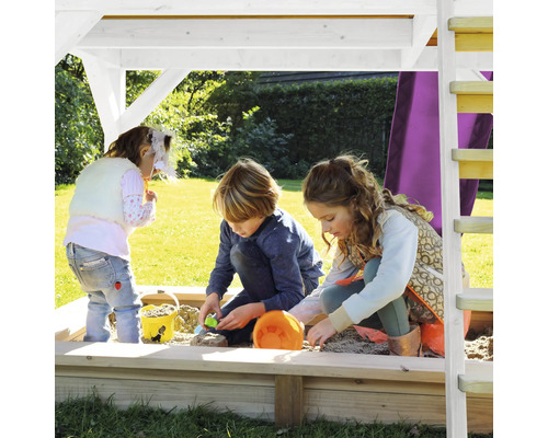 Kinder spielen in einem Sandkasten mit Dach und Leiter im Garten.