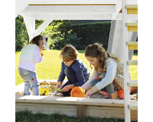 Kinder spielen im Sandkasten mit Dach und Leiter im Garten.