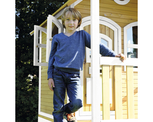 Junge steht vor einem Holzspielhaus mit offenen Fenstern und Geländer