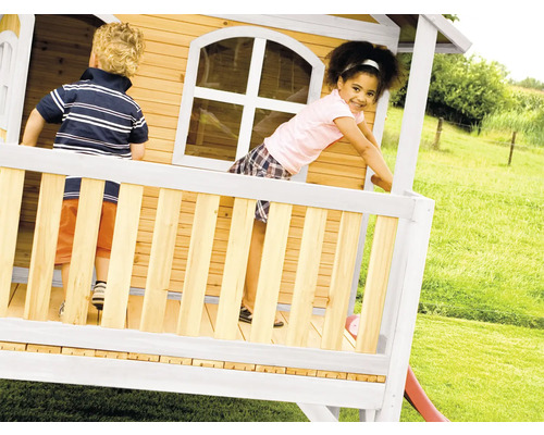 Kinder spielen in einem Holzspielhaus mit Rutsche im Garten.