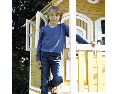 Junge steht vor einem Holzspielhaus mit geöffneten Fenstern.