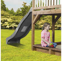 Kind sitzt im Sandkasten eines Spielhauses mit Rutsche im Garten.