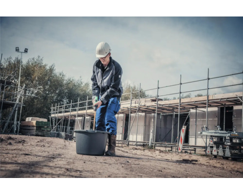 Bauarbeiter mischt Material in einem Eimer mit einem Rührgerät auf einer Baustelle.