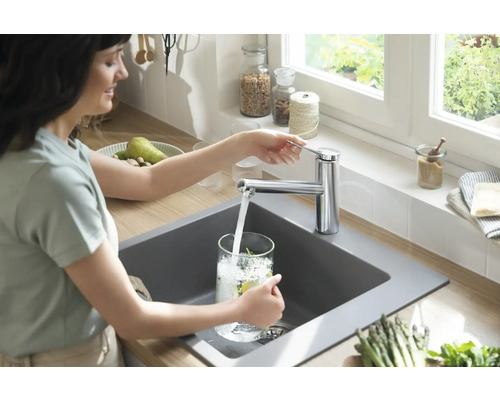 Frau füllt Glas mit Wasser am Spültisch mit Armatur in der Küche