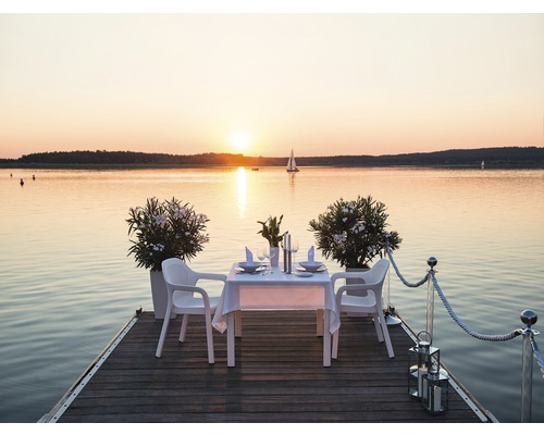 Ein gedeckter Tisch mit Stühlen auf einem Holzsteg mit Blick auf einen See bei Sonnenuntergang.
