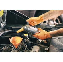 Eine Person füllt mit Handschuhen Öl mit einem Trichter in einen Motor