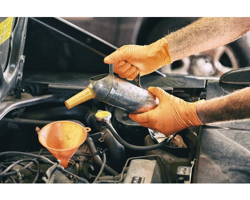 Eine Person füllt mit Handschuhen Öl mit einem Trichter in einen Motor