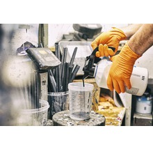 Eine Person mit Handschuhen gießt Farbe in einen Messbecher.