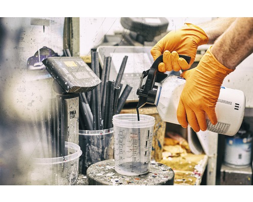 Eine Person mit Handschuhen gießt Farbe in einen Messbecher.