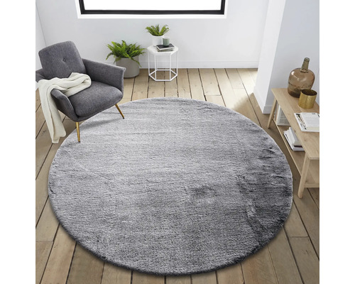 Runder grauer Teppich im Wohnzimmer mit Sessel und Beistelltisch.