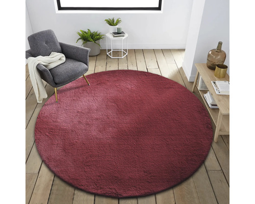 Innenraum mit rundem, bordeauxfarbenem Teppich, Sessel, Beistelltisch und Holzregal
