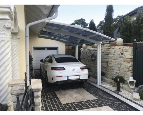 Carport mit Auto auf gepflasterter Auffahrt vor Wohnhaus.