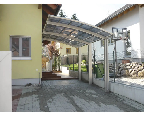 Carport aus Aluminium mit transparenter Überdachung neben einem Wohnhaus.