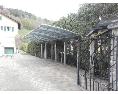 Carport mit Metallstruktur und Glasdach neben einem Haus.