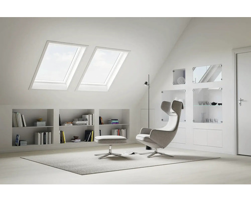 Helles Dachzimmer mit Dachfenstern, Regalen und Sessel mit Fußhocker