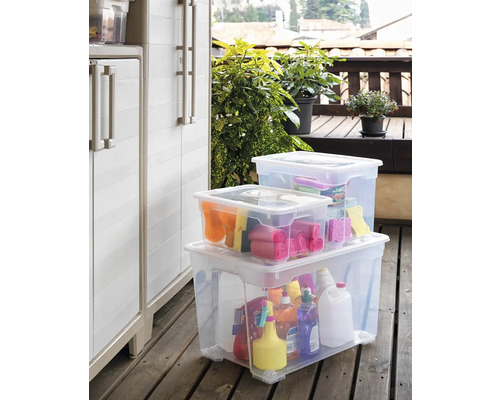 Szene mit drei transparenten Aufbewahrungsboxen auf einer Holzterrasse, gefüllt mit verschiedenen Gegenständen und Reinigungsmitteln, neben einem Lagerschrank.