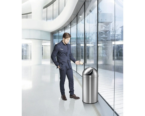 Mann wirft Becher in einen Edelstahl Abfalleimer in modernem Gebäude.