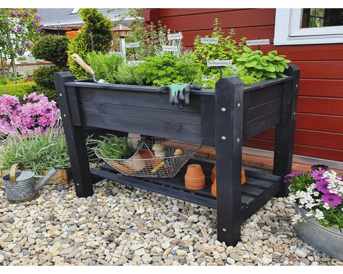Hochbeet aus Holz mit Kräutern, Gartengeräten und Ablagefläche im Garten.