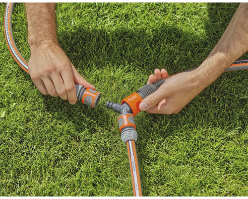 Zwei Hände verbinden einen Gartenschlauch mit einem Y-Verteiler auf einer Rasenfläche.