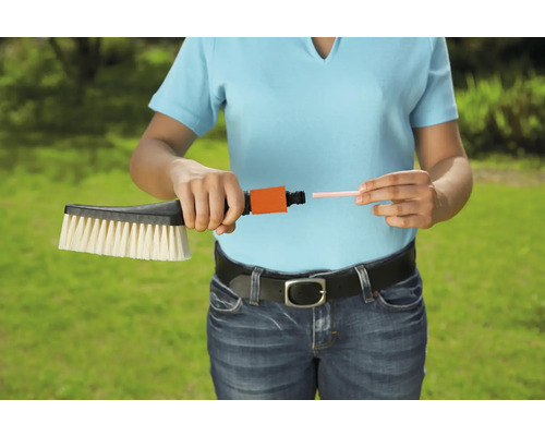 Eine Frau schliesst eine Waschbürste an einen Schlauchanschluss an.