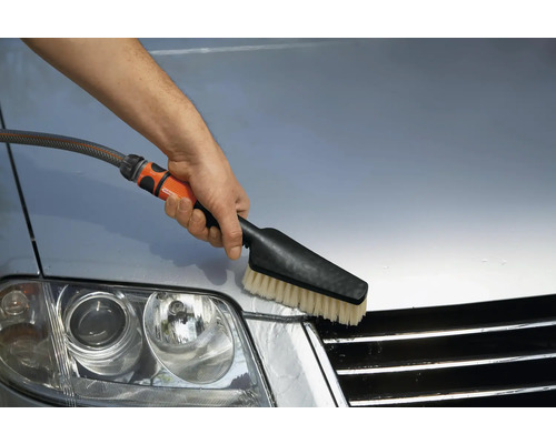 Eine Person reinigt ein Auto mit einer Waschbürste.