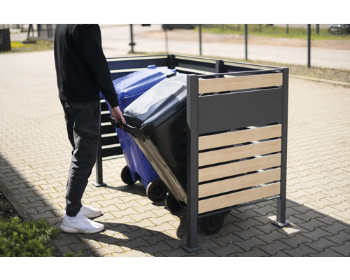 Person schiebt Mülltonne in Mülltonnenbox aus Metall und Holz