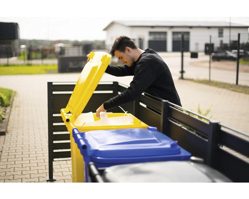 Mann wirft Papier in eine gelbe Wertstofftonne im Freien.