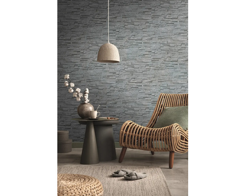 Dekoratives Wohnzimmer mit Rattansessel, Steintapete, Beistelltisch, Lampe und Teppich für ein gemütliches Ambiente