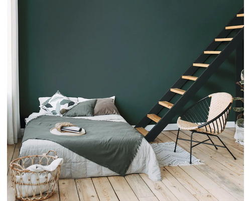 Schlafzimmer mit Bett, Leiter und Rattansessel auf Holzboden