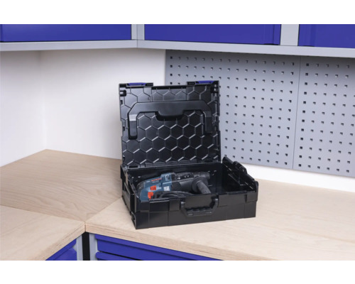 Geöffnete schwarze Werkzeugkiste mit Bohrmaschine auf einer Werkbank