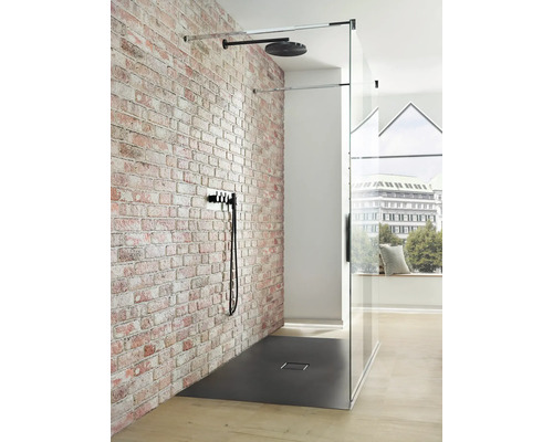 Begehbare Dusche mit Kopfbrause, Armatur und Duschwanne vor Ziegelwand