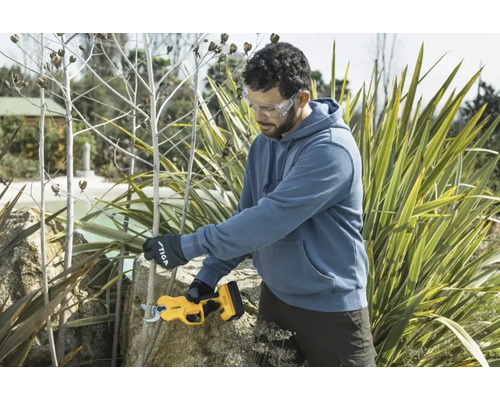 Ein Mann beschneidet mit einer Akku-Gartenschere Pflanzen im Garten. Er trägt dabei eine Schutzbrille und Gartenhandschuhe.