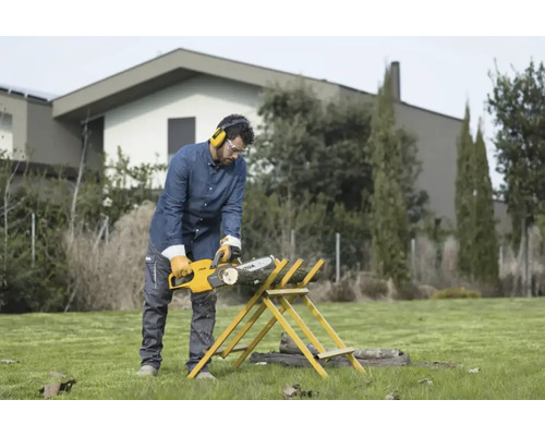 Mann mit Gehörschutz und Schutzbrille sägt mit einer Kettensäge Holz auf einem Sägebock im Garten.
