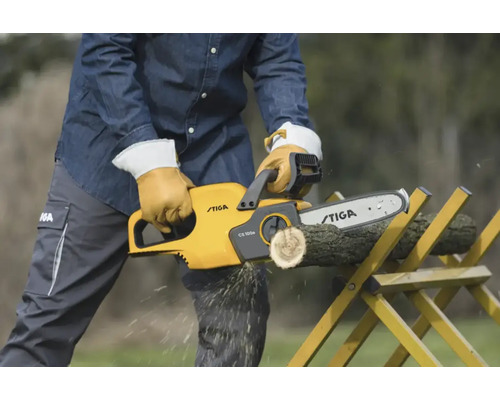 Eine Person sägt mit einer gelben Stiga Kettensäge ein Holzstück, das auf einem gelben Sägebock liegt.