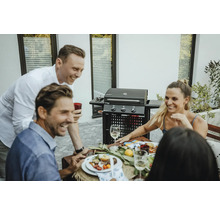 Personen sitzen an einem Tisch mit einem Grill im Hintergrund