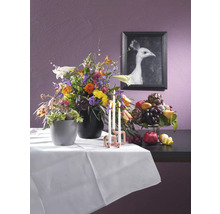 Dekoratives Stillleben mit Blumenarrangement, Obstschale und Kerzen auf einem Tisch mit weißer Tischdecke, an der Wand ein Bild