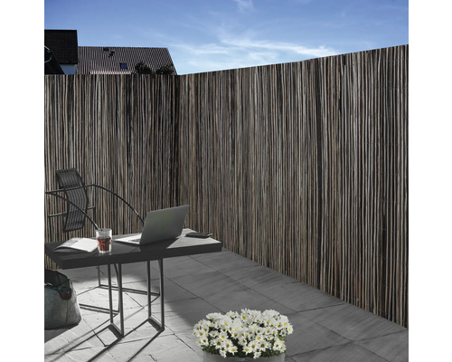 Sichtschutzzaun aus Naturmaterial neben einem Gartentisch mit Laptop im Außenbereich.