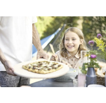 Vater serviert Pizza für ein lächelndes Mädchen im Garten.