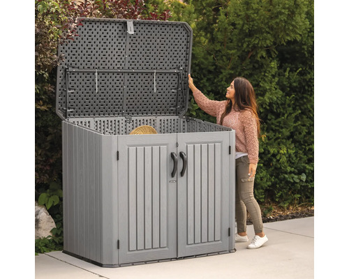 Grauer Gartenschrank mit geöffnetem Deckel und Türen vor einer Frau im Garten