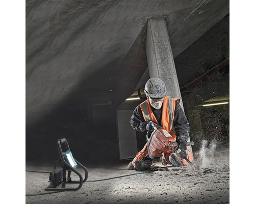 Ein Bauarbeiter benutzt einen Abbruchhammer in einer Betongrube, beleuchtet von einer Arbeitsleuchte.