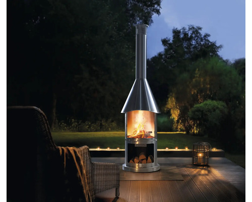 Edelstahl-Terrassenkamin mit Holz auf einer Holzterrasse mit Garten im Hintergrund