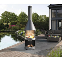 Außenbereichszene mit einem runden Holzkohlegrillkamin auf einer Terrasse mit Sitzgelegenheiten im Hintergrund