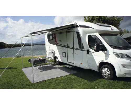 Wohnmobil mit Markise, Tisch, Stühlen und Bodenschutzmatte auf einer Wiese am See