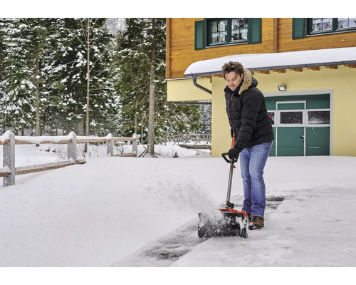 Ein Mann benutzt eine Schneefräse vor einem Haus im Winter.