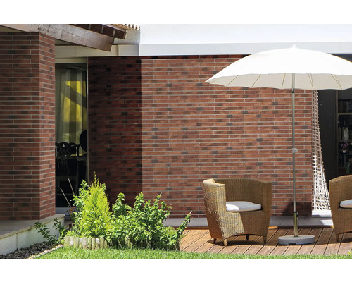 Terrasse mit Ziegelwand, Sonnenschirm und Korbsesseln.