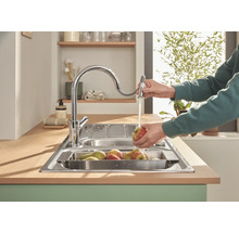 Spültisch mit Wasserhahn und Person beim Abwaschen von Obst in der Küche