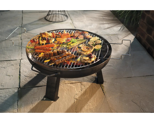 Runder Grill mit Grillgut wie Fleisch, Gemüse und Spießen auf einem Steinboden